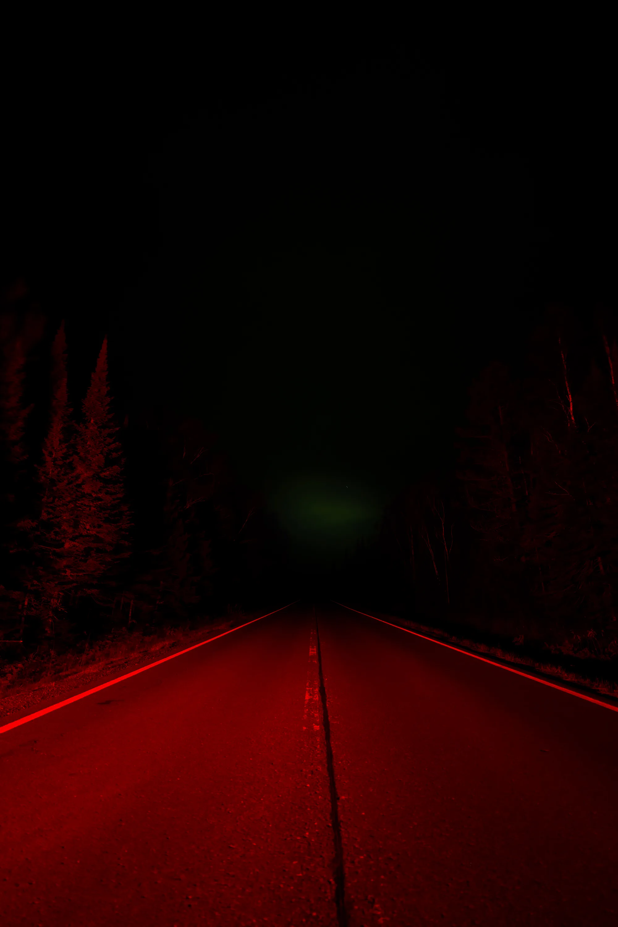 faint glow of the northern lights over a brake light glow on a road
