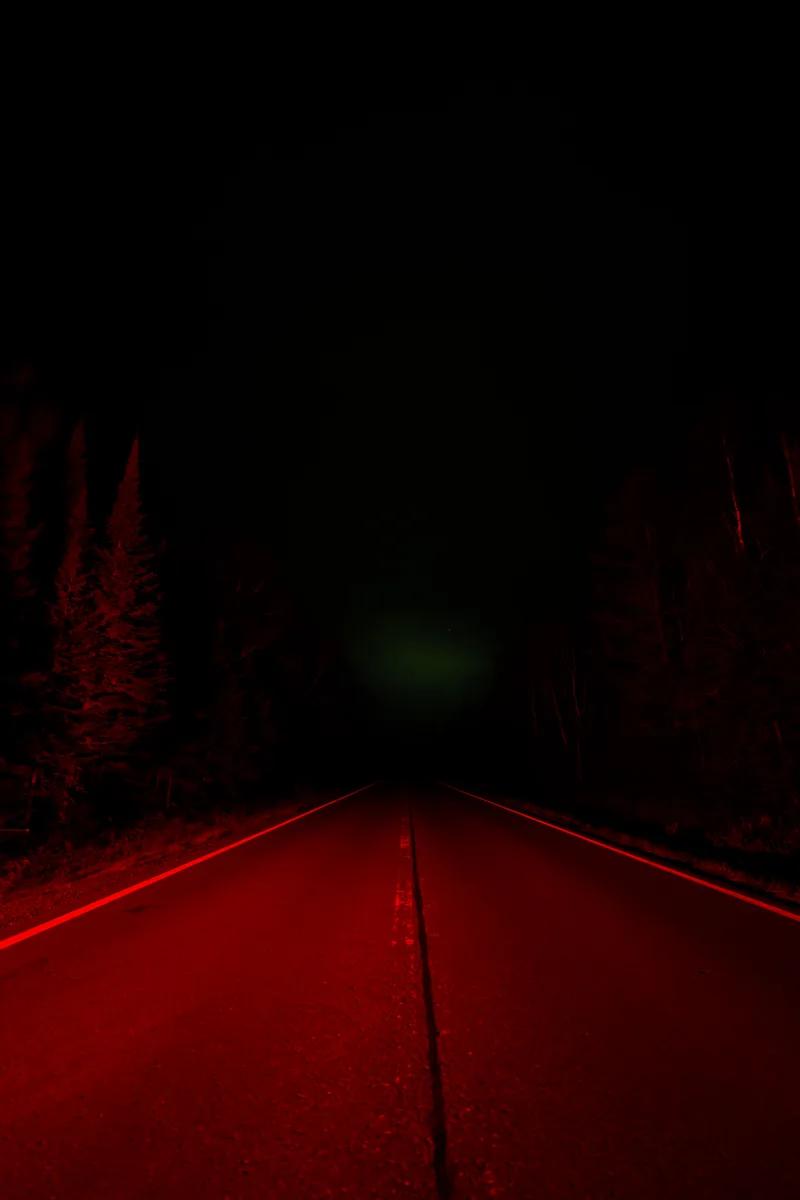 faint glow of the northern lights over a brake light glow on a road