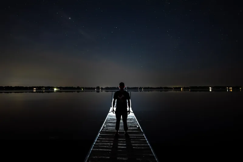 man standing in front of a light on a night time pier with the stars out