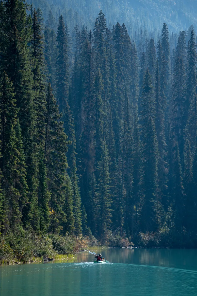 lone canoe paddling around the shoreline of emerald lake