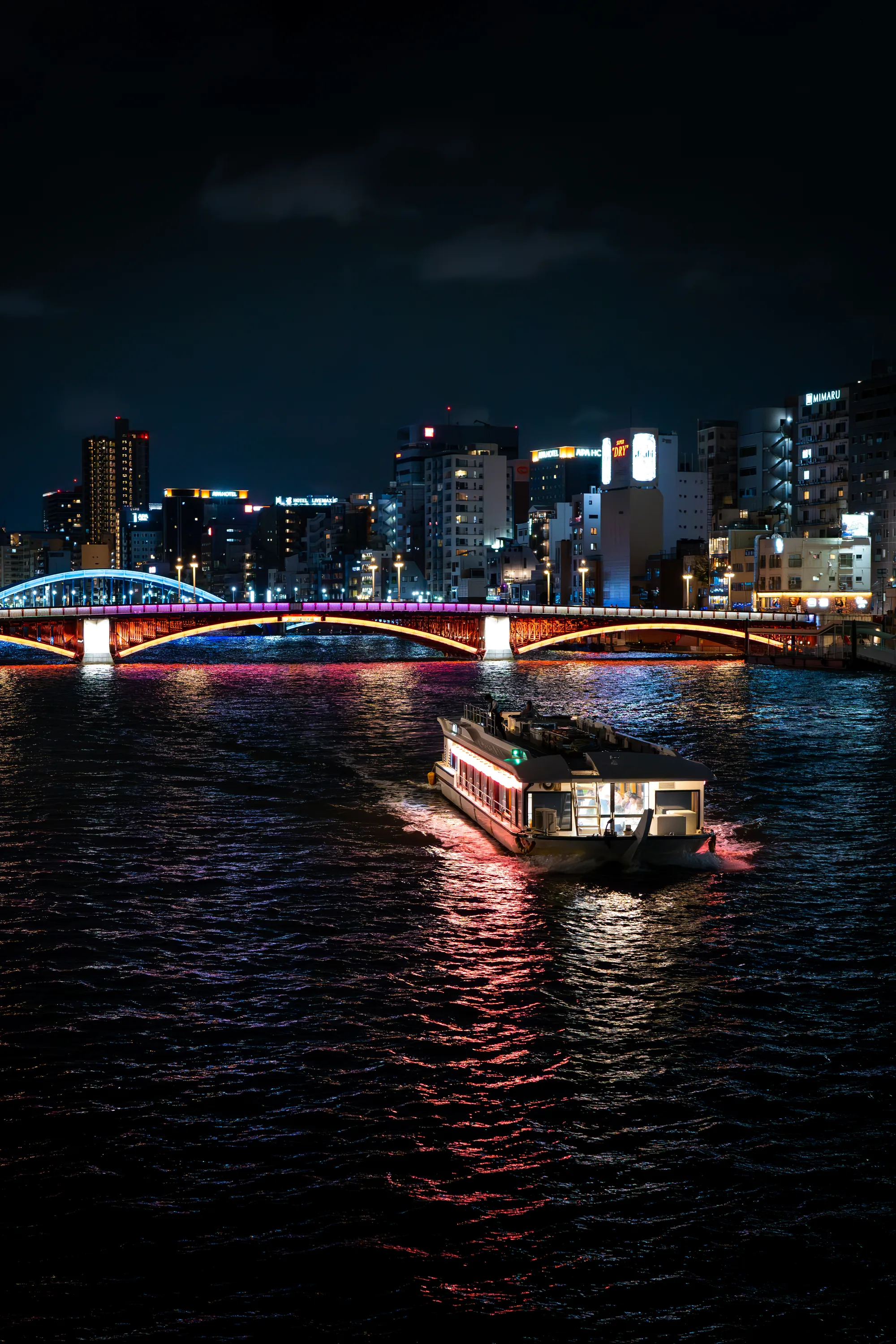 night shot of the sumida river in tokyo japan with colorful bridge lights and a passenger boat