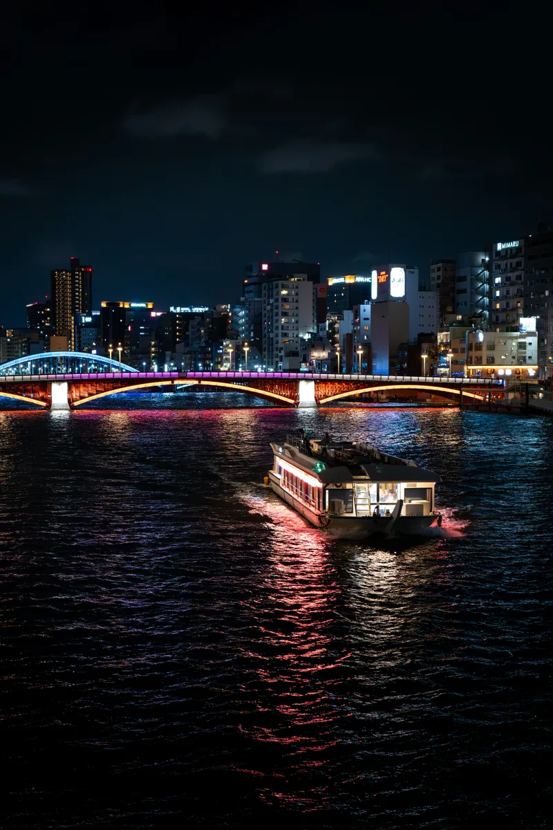 night shot of the sumida river in tokyo japan with colorful bridge lights and a passenger boat