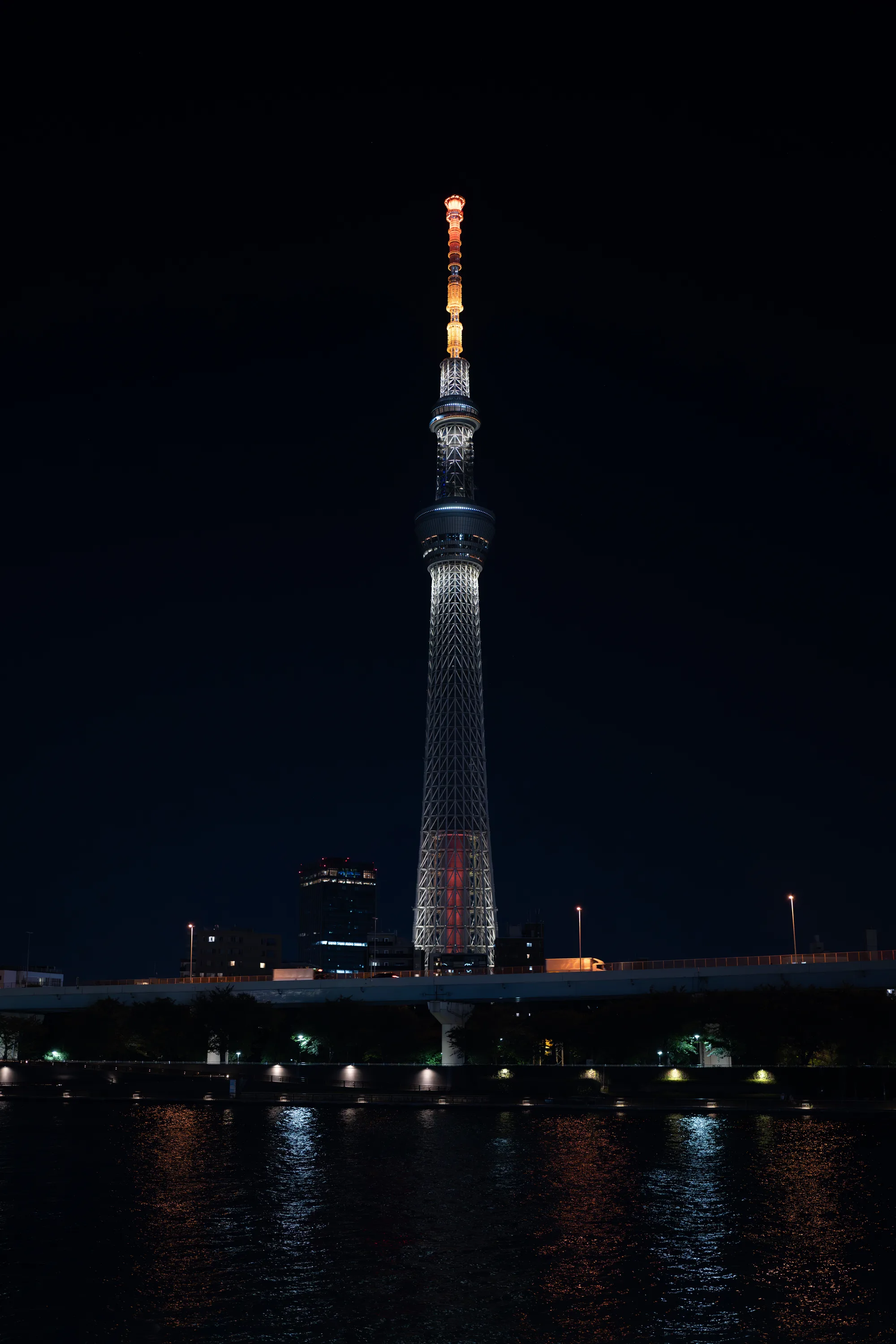 tokyo skytree lit up at night from a distance away across a river in tokyo japan