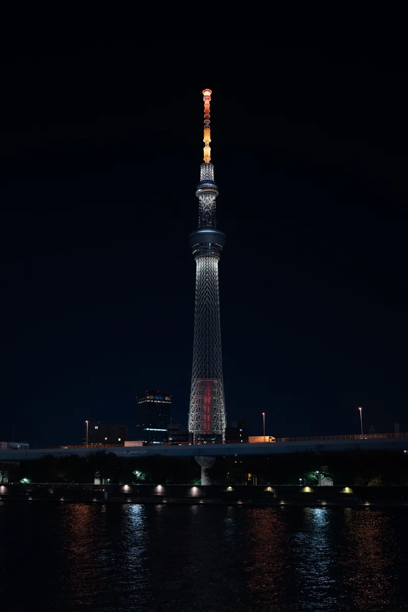 tokyo skytree lit up at night from a distance away across a river in tokyo japan